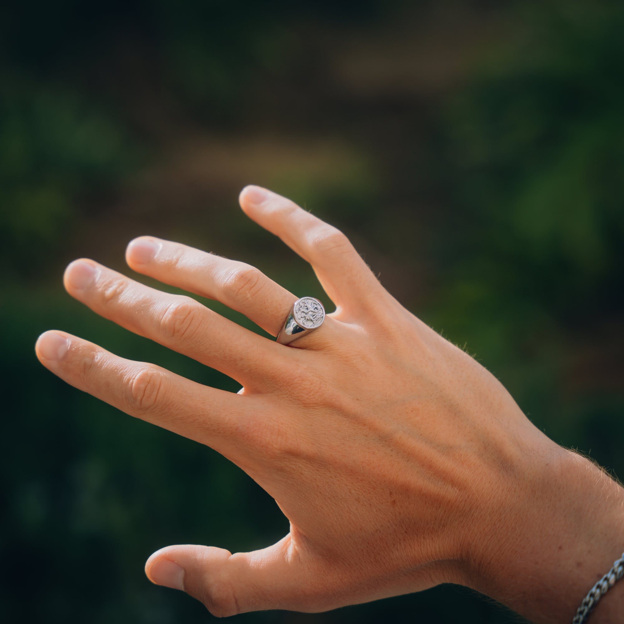 Hand wearing a silver ring with a diamond on a blurred green background