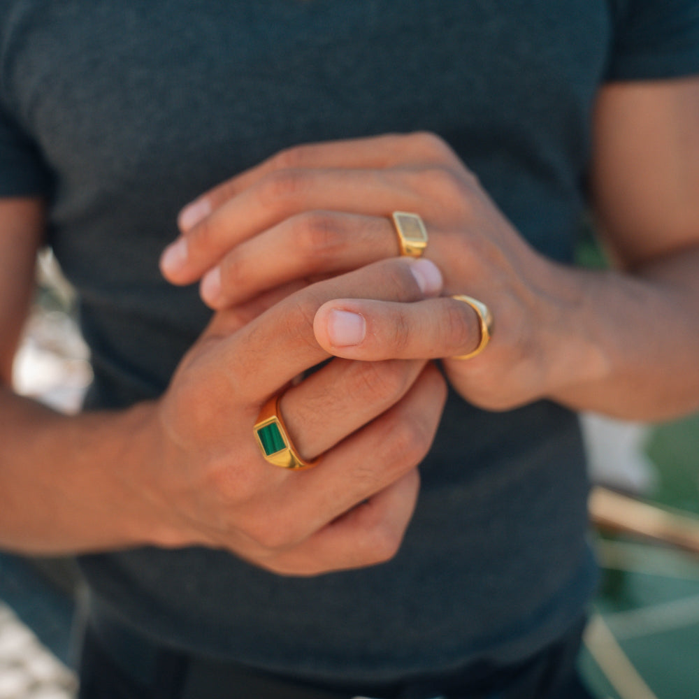 Close-up of hands with gold rings featuring green gemstones, wearing a dark shirt.
