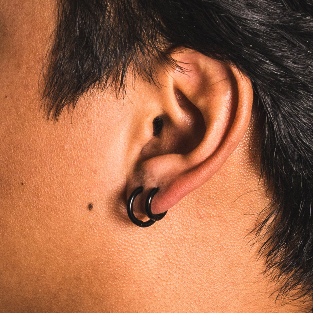 Close-up of an ear with a black hoop earring on a blurred background