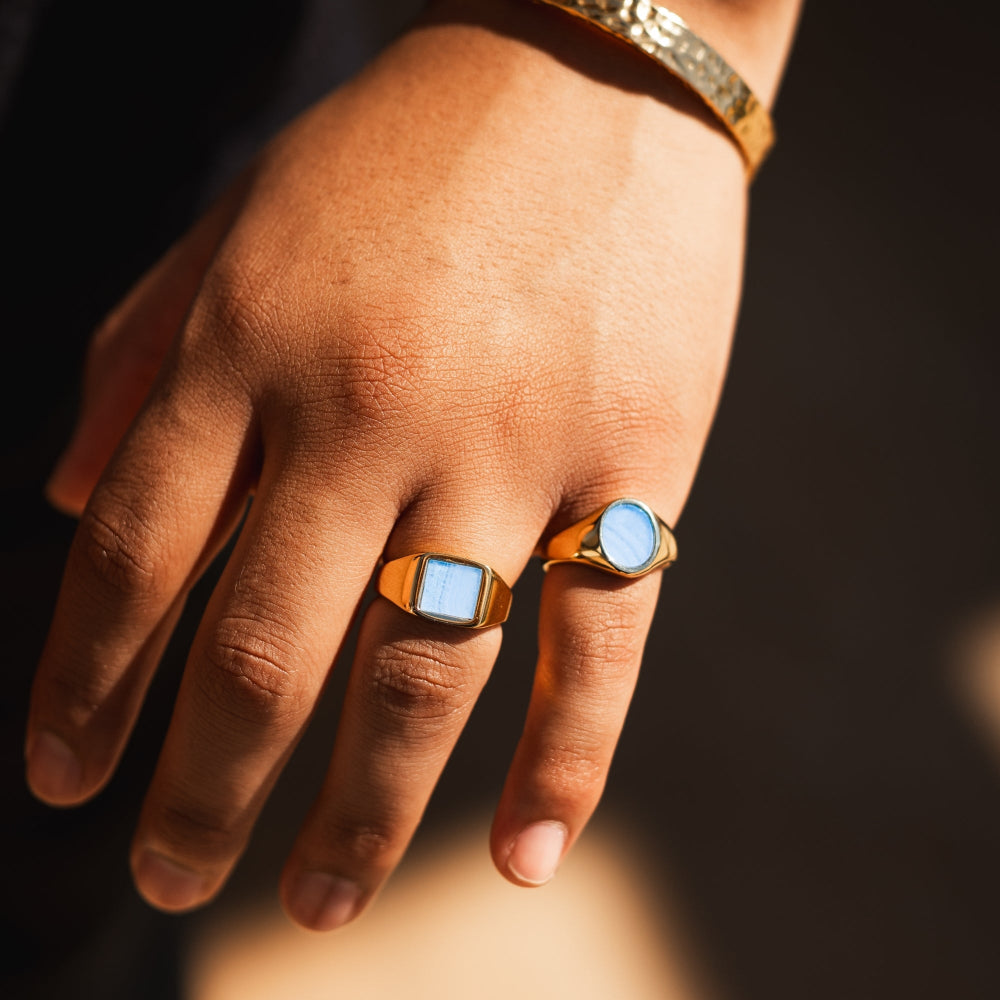 Hand wearing two gold rings with blue stones on a dark background