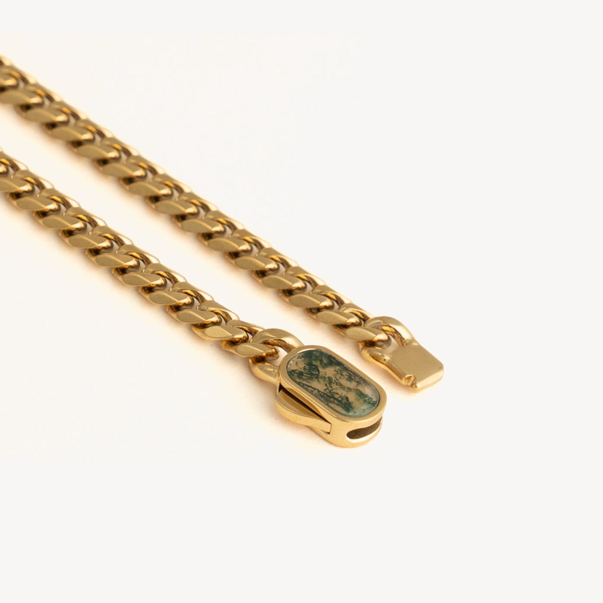 Gold chain with a green stone clasp on a white background