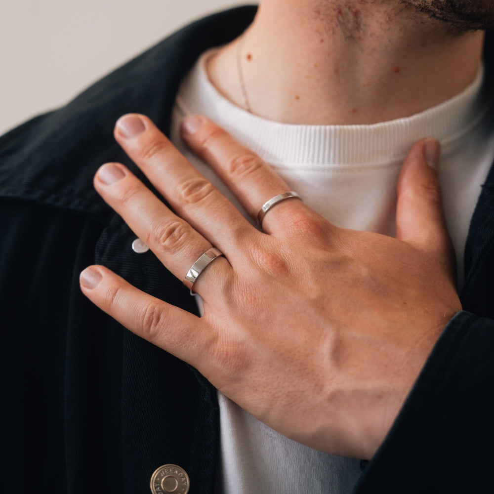 Close-up of a person wearing two rings on their fingers, with a neutral background.