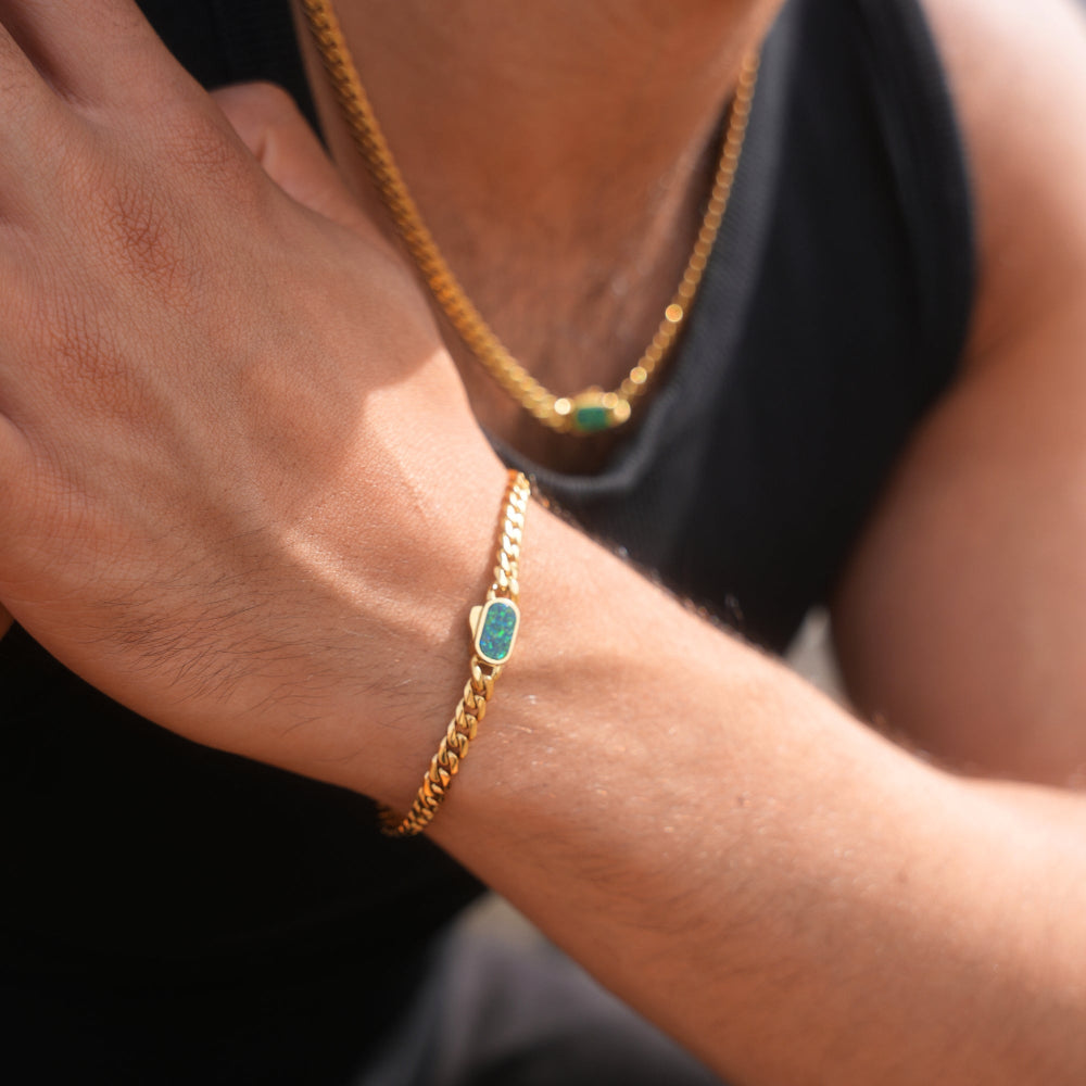 Gold bracelet with a green gemstone on a wrist against a dark background