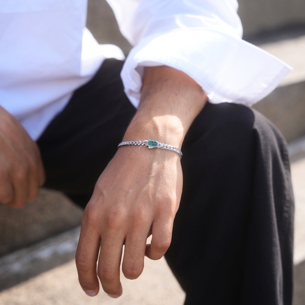 Person wearing a silver bracelet with a green stone on a blurred outdoor background