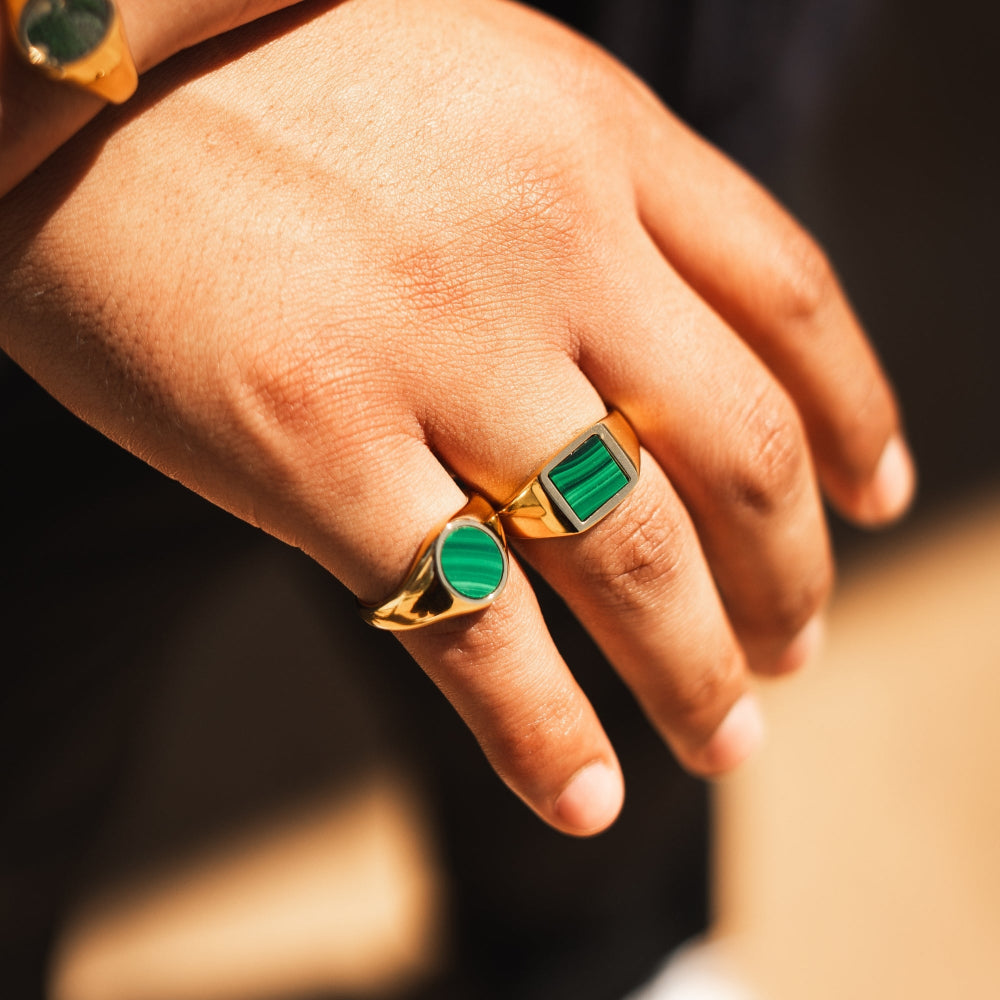 Hand wearing two gold rings with green gemstones on a blurred background
