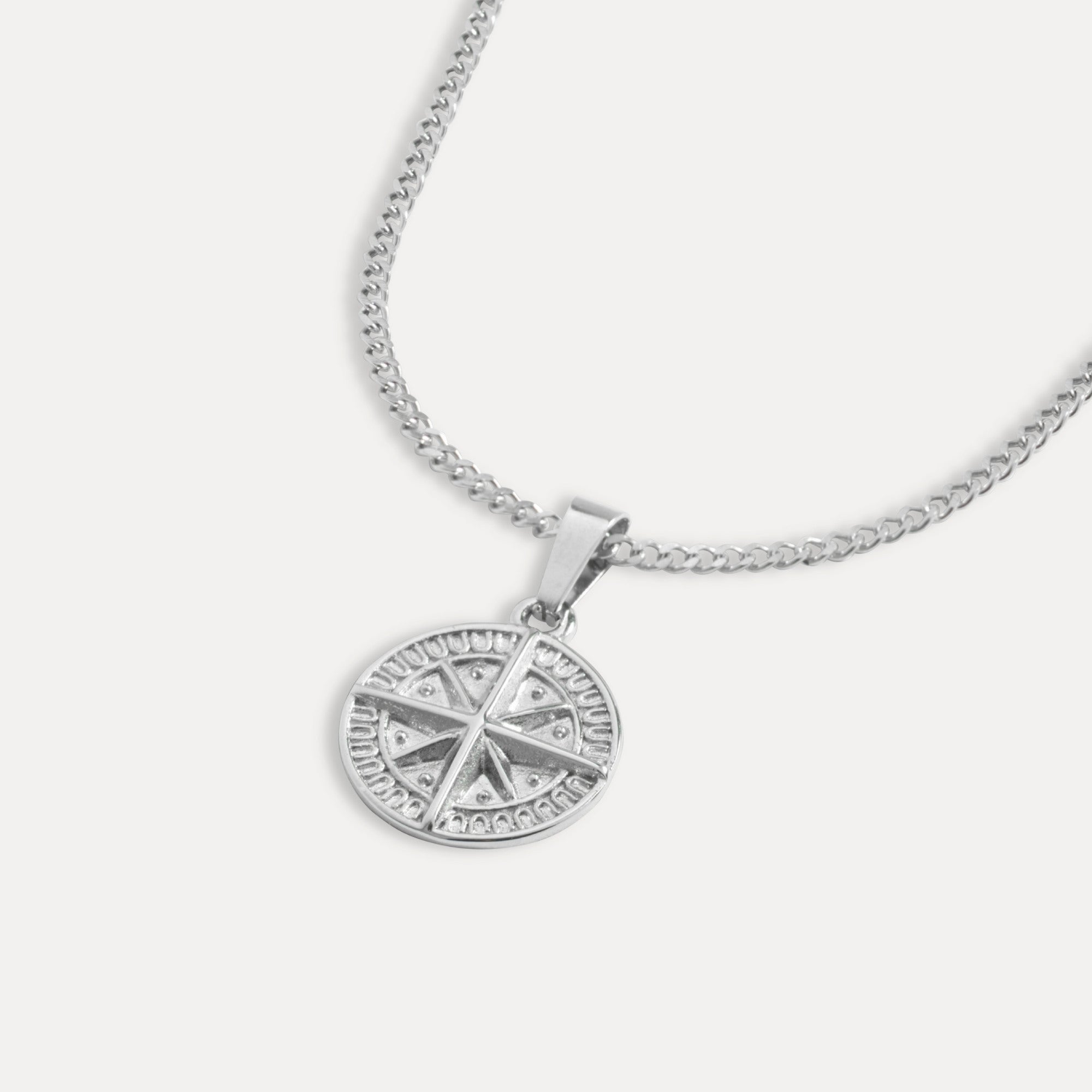 A silver compass pendant necklace with a detailed design on the pendant and a thin rope chain.