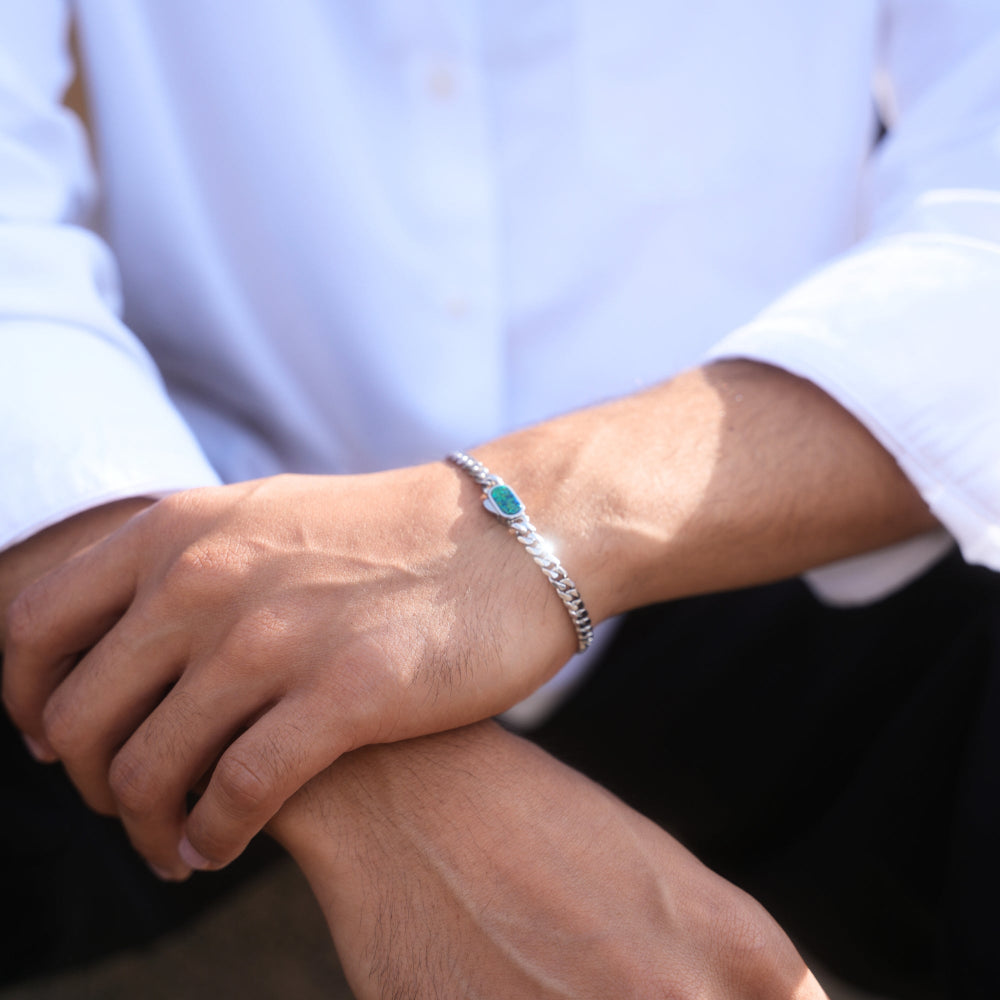 Close-up of a wrist wearing a silver bracelet with a turquoise stone, against a blurred background.