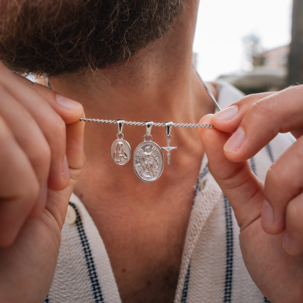 Person holding a silver necklace with three pendants outdoors