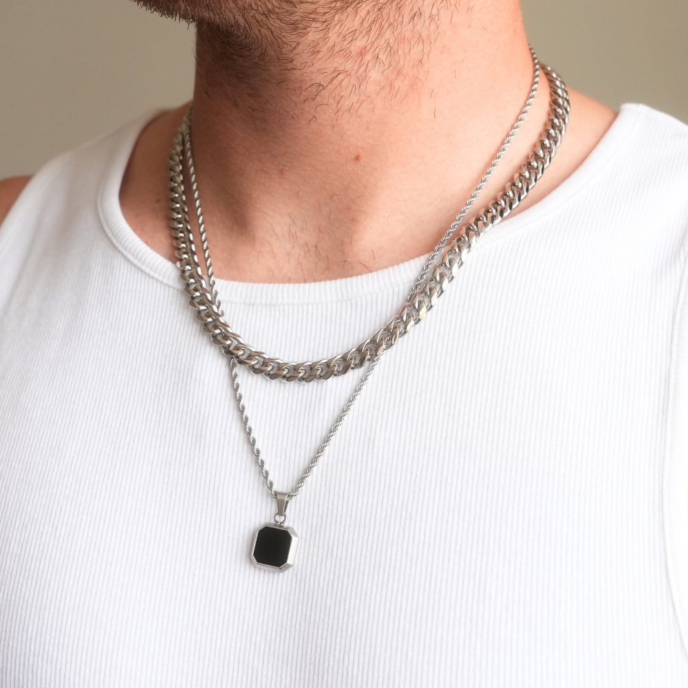 Person wearing a silver chain necklace with a black pendant on a plain background