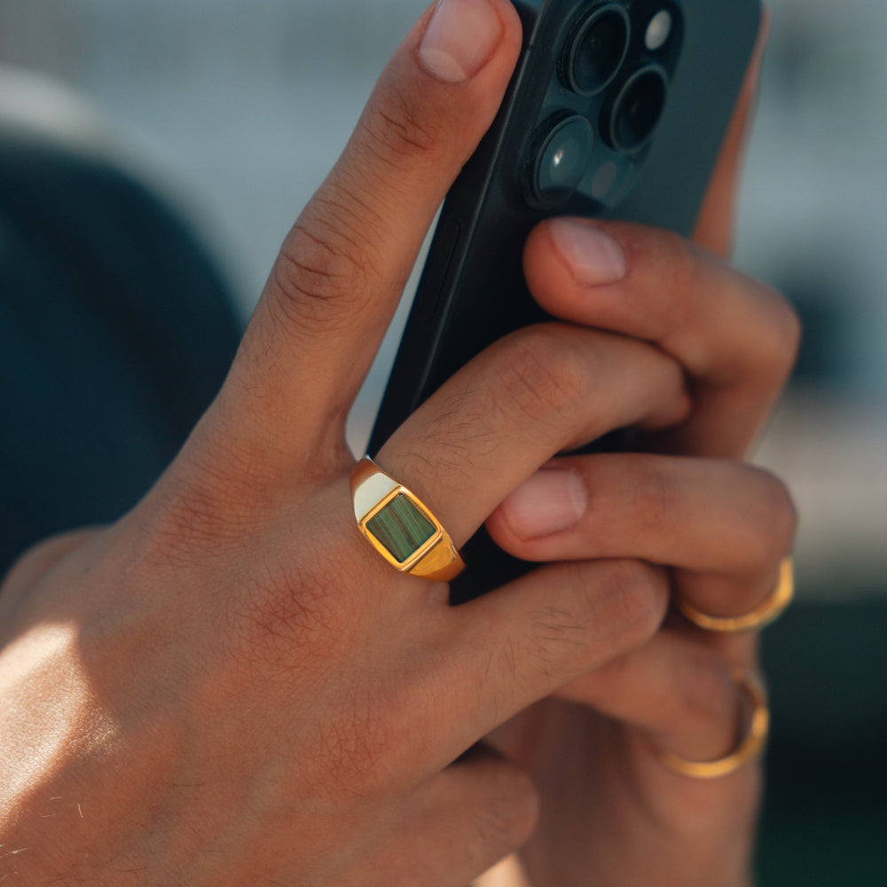 Hand holding a smartphone with a gold ring featuring a digital display.