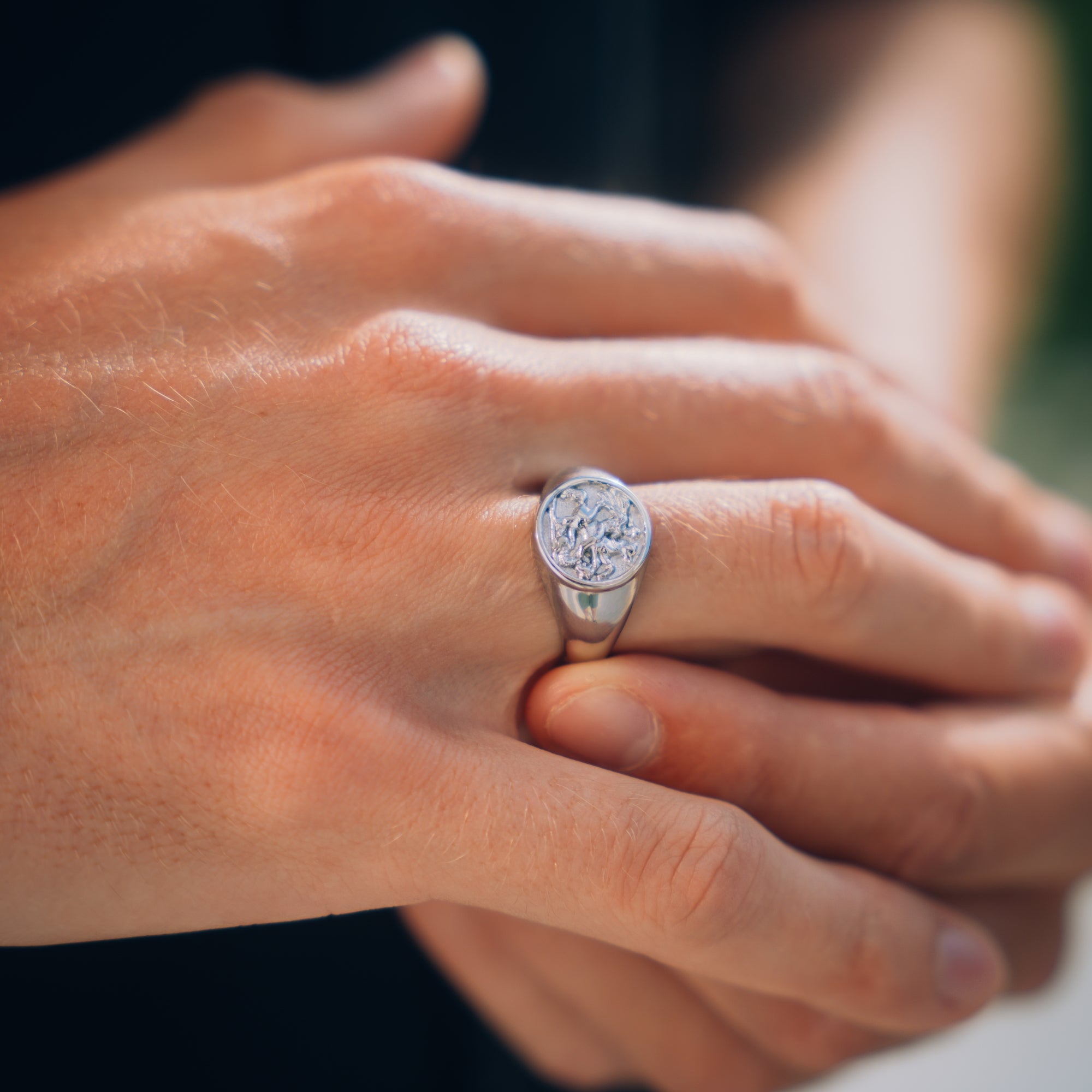 Close-up of a hand wearing a silver ring with a diamond on a blurred background