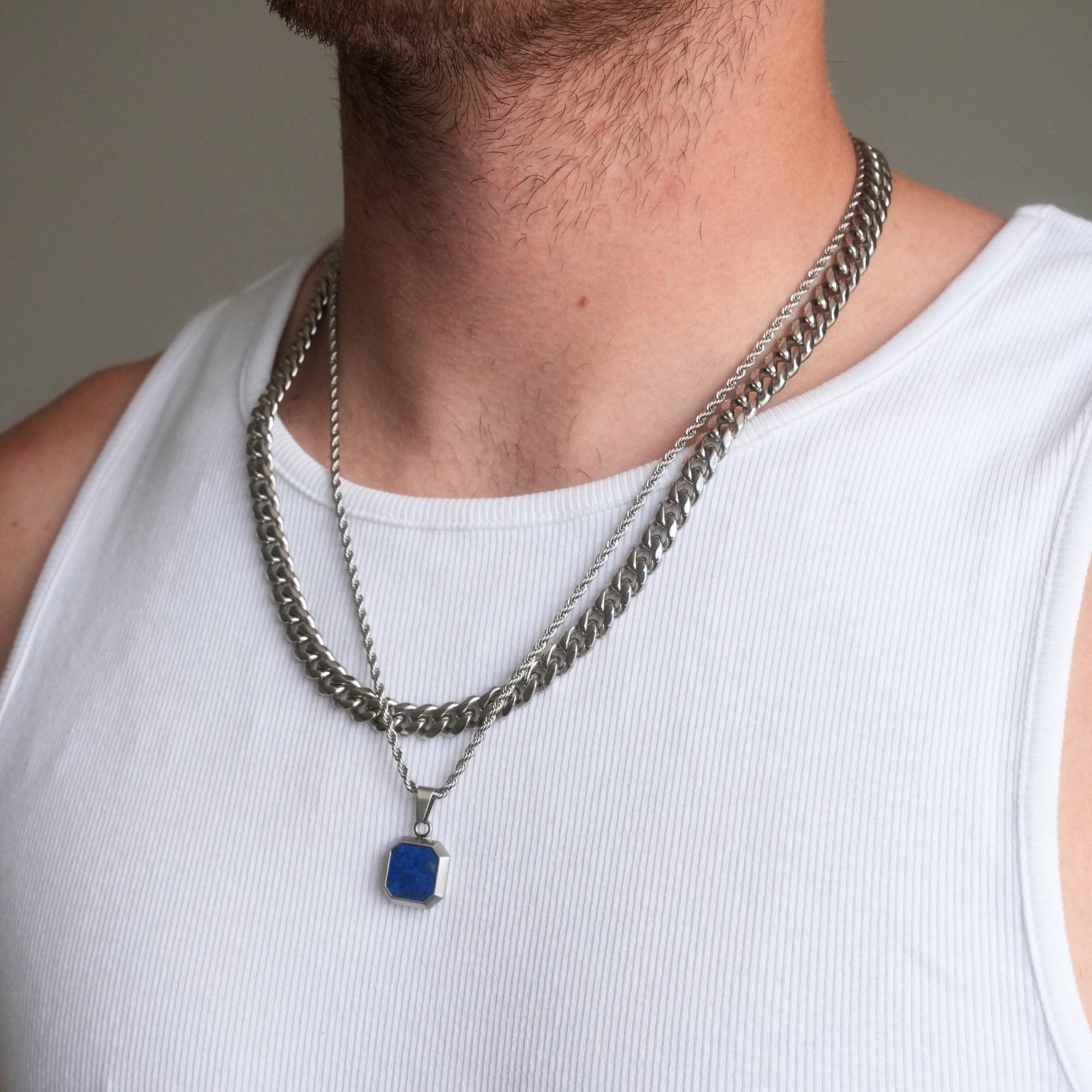 Person wearing a silver chain necklace with a blue pendant on a plain background