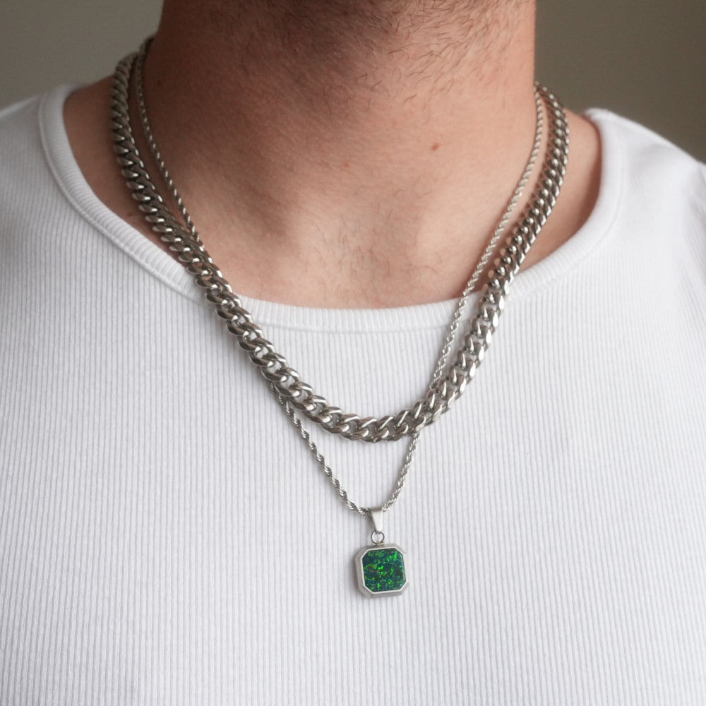 Person wearing a silver chain necklace with a green pendant on a white background