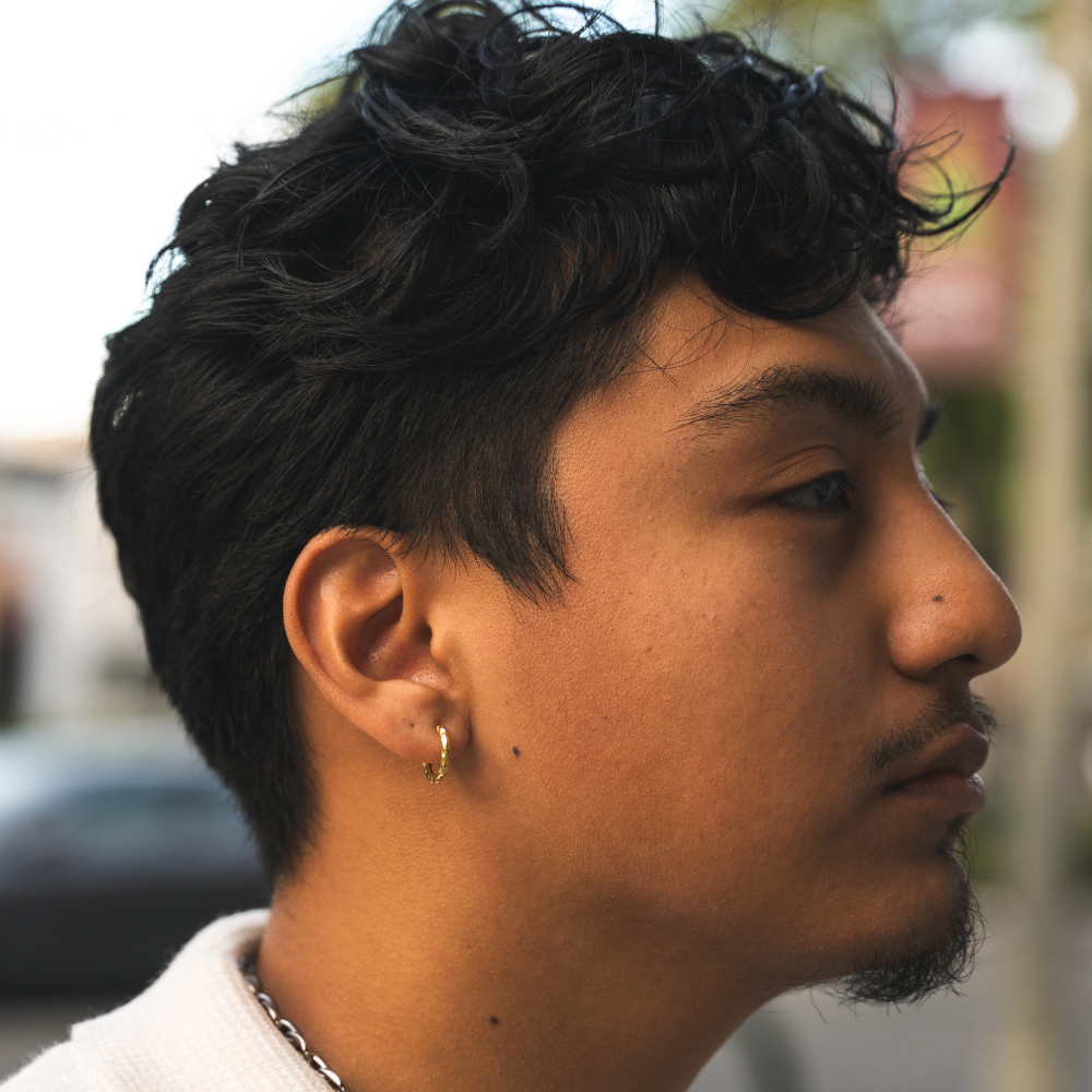 A person viewed from the side wearing a gold-colored hammered hoop earring.