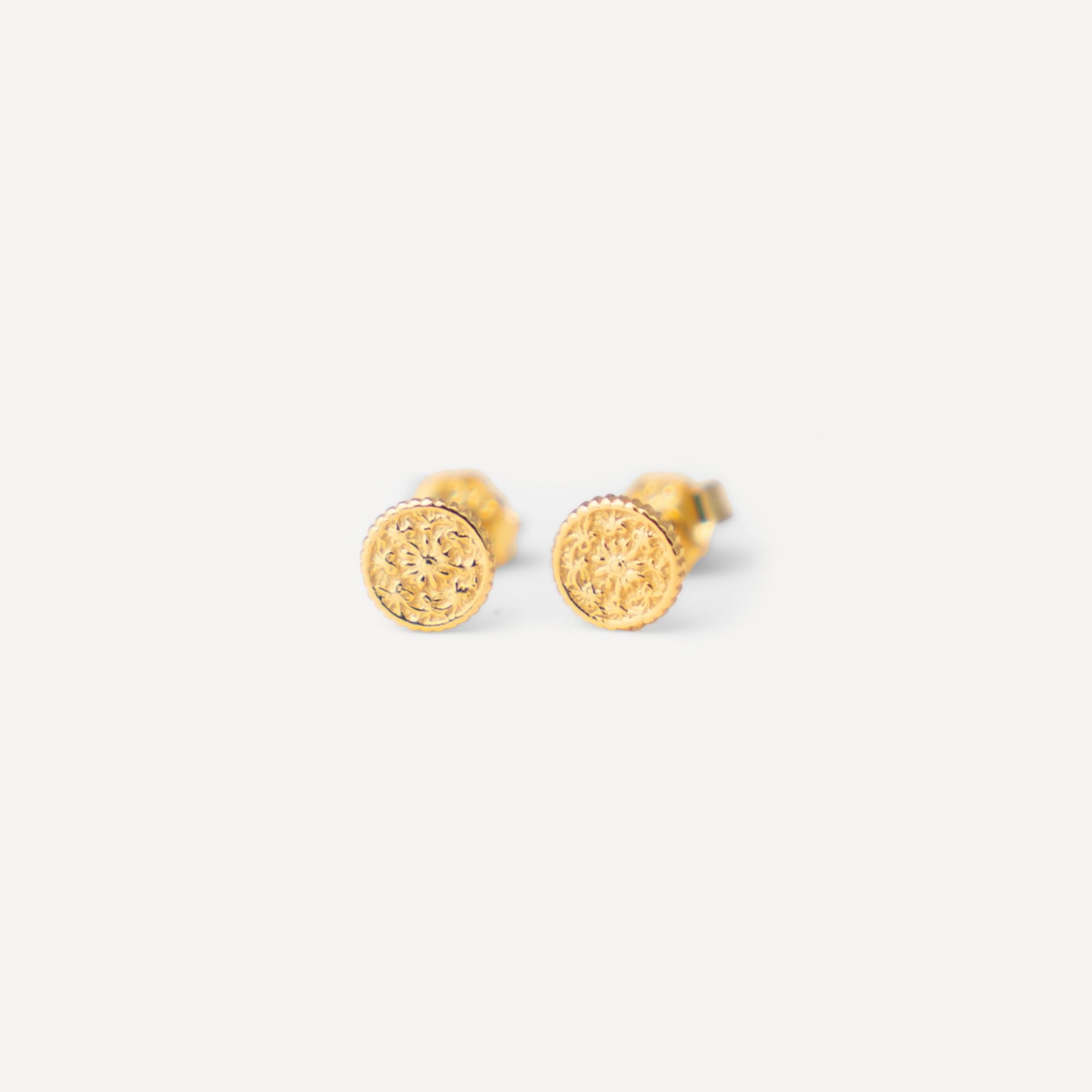 A pair of small round gold stud earrings with a textured, hammered surface, shown on a clean off-white background.