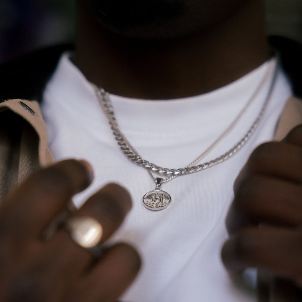 Person wearing a silver chain necklace with a pendant, hands clasped together.