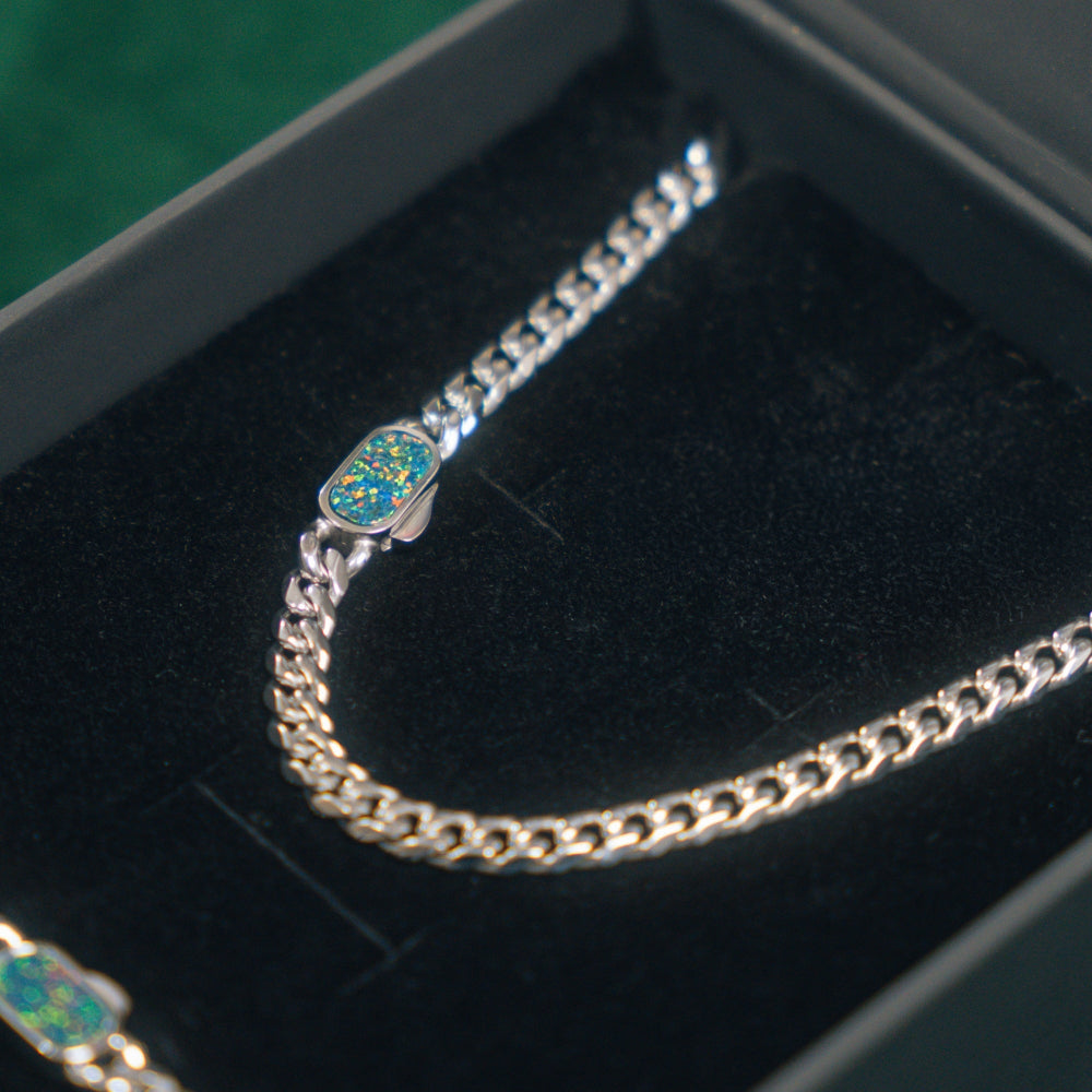 Silver chain bracelet with a blue gemstone clasp on a black velvet surface