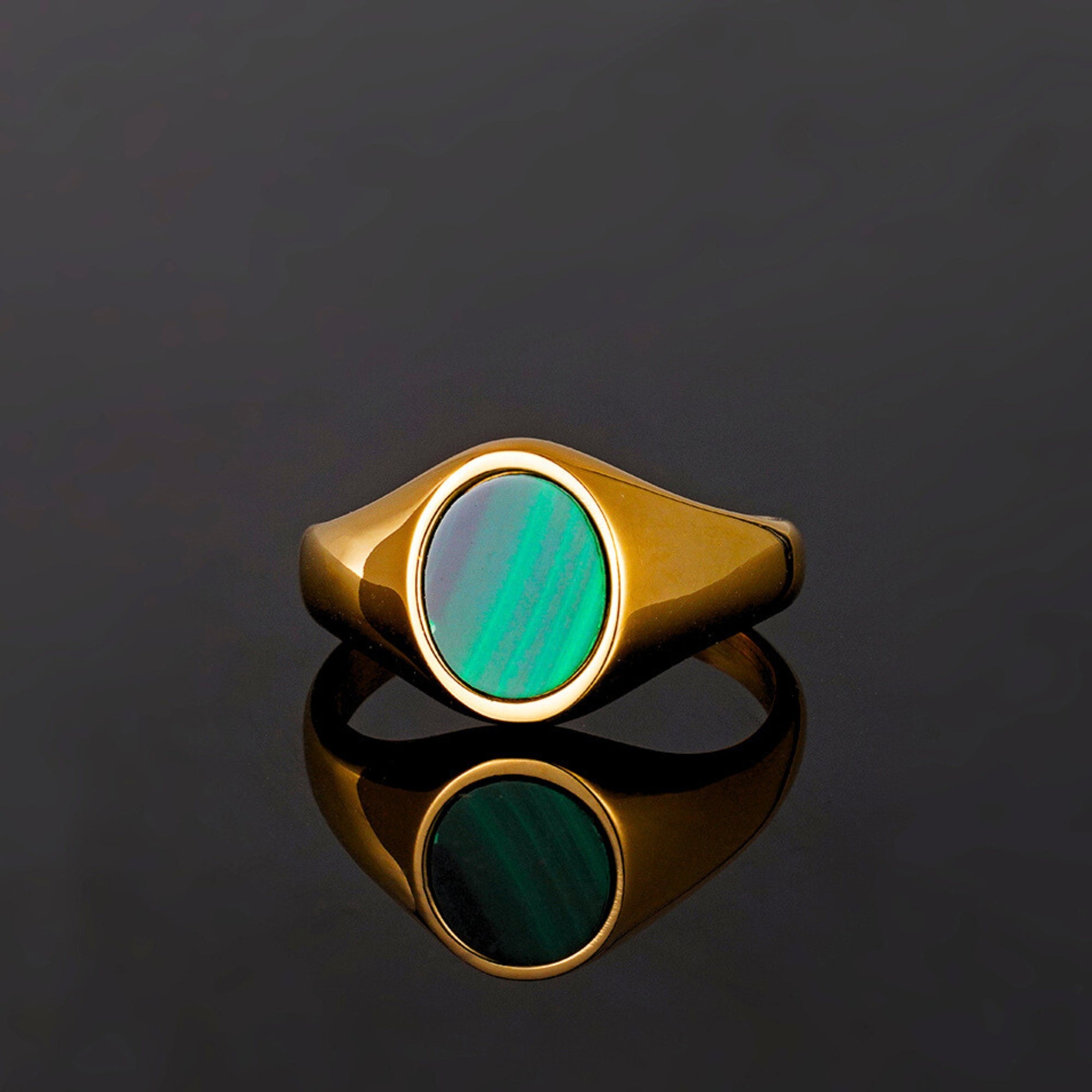 Gold ring with a green stone on a reflective black surface