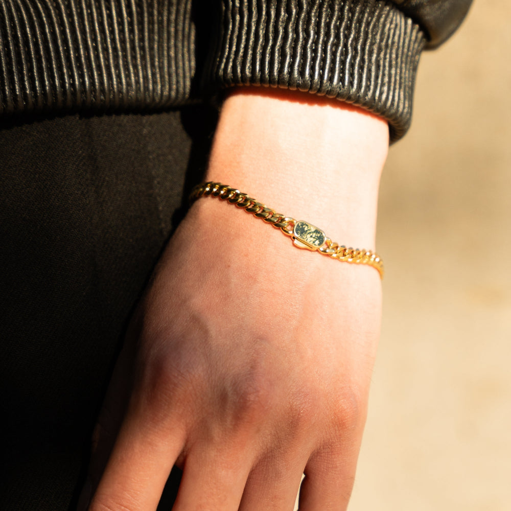 Gold bracelet with a green gemstone on a wrist against a blurred background