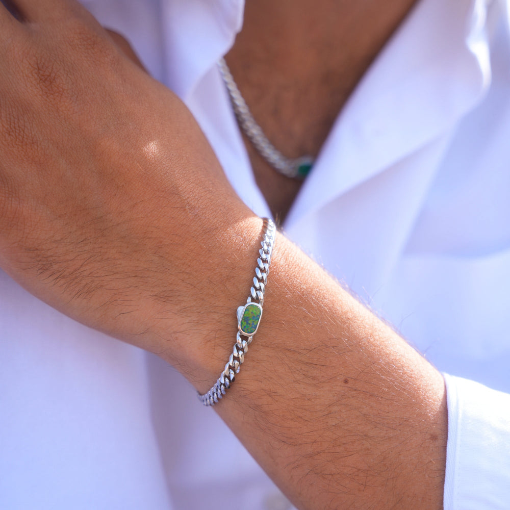 Close-up of a wrist wearing a silver bracelet with a green stone on a white background