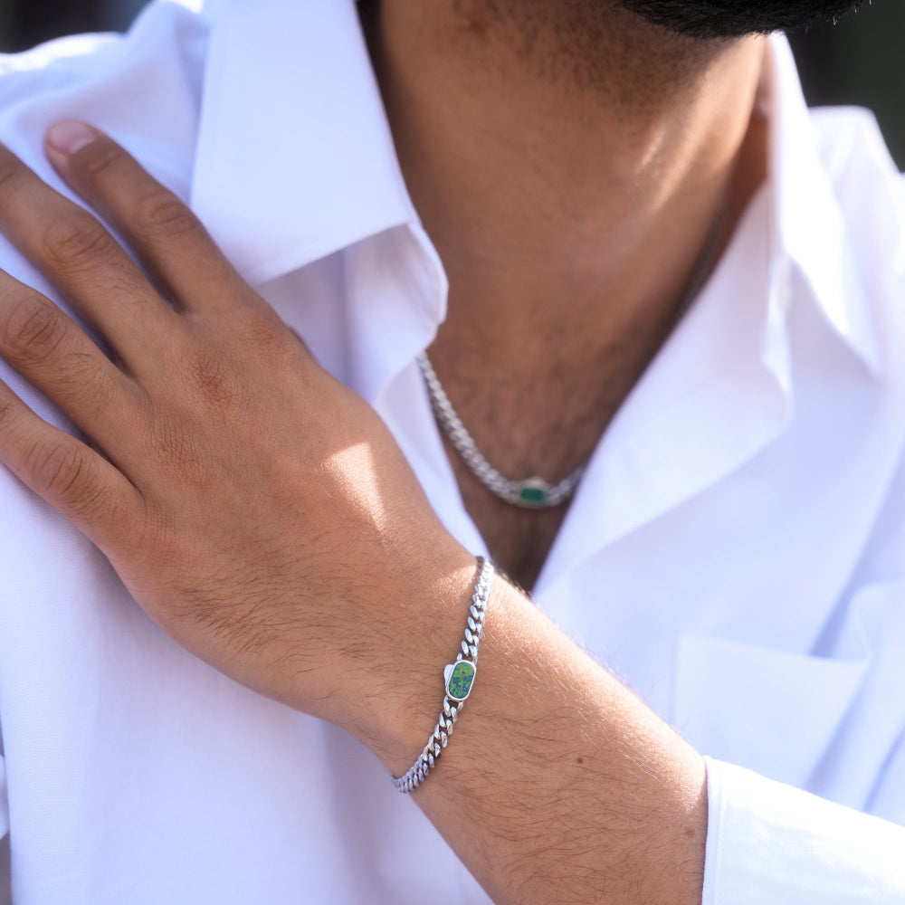 Close-up of a person wearing a silver bracelet with a green gemstone on a white shirt.