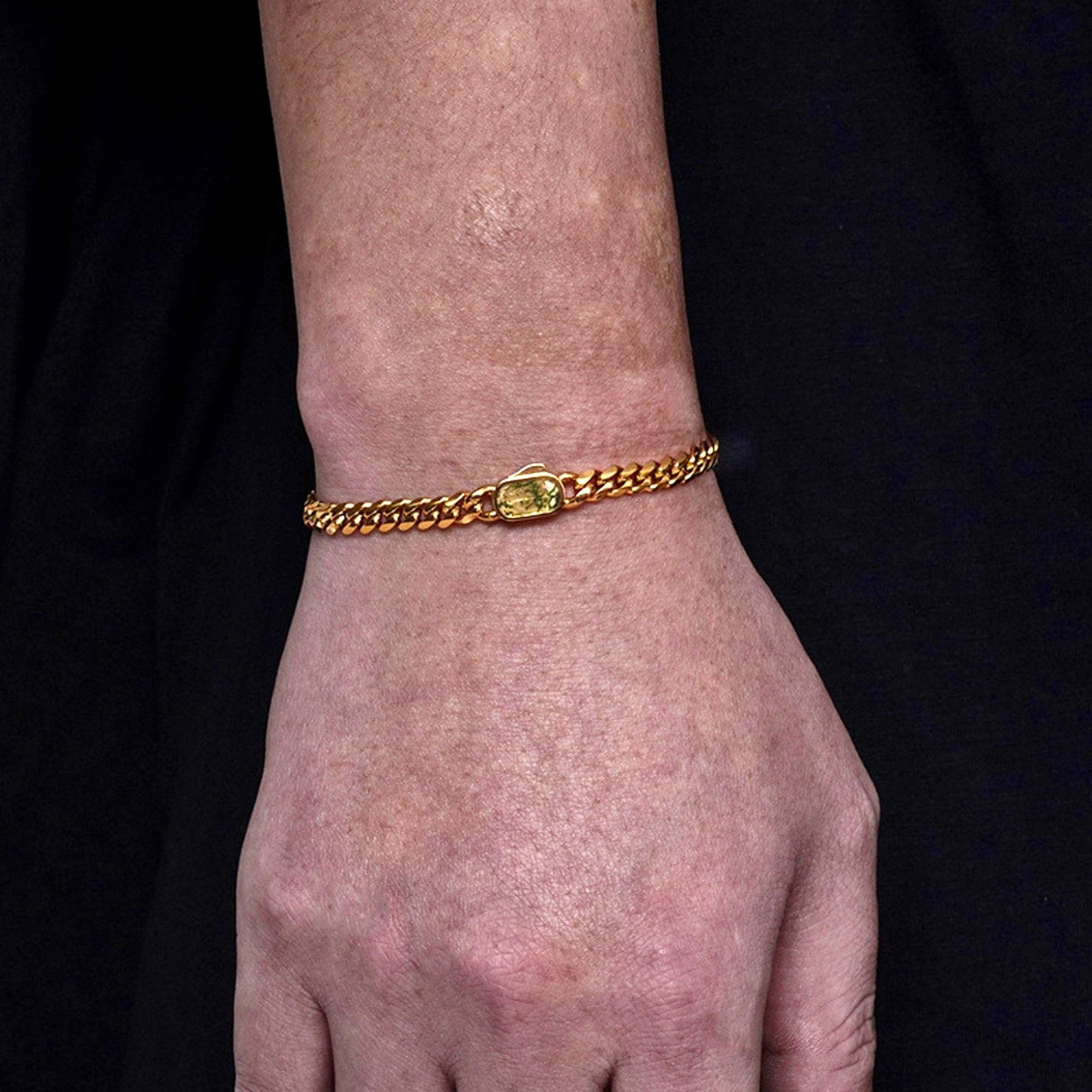 Hand wearing a gold bracelet with a green gemstone on a black background