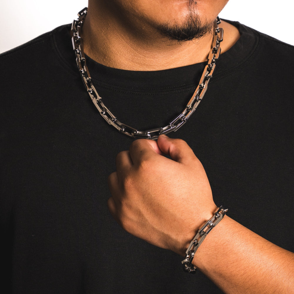 Person wearing a black shirt with a chain necklace and bracelet on a white background