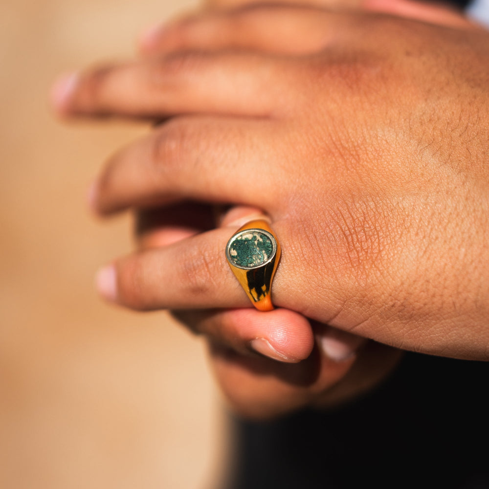 Close-up of a hand wearing a gold ring with a green stone on a blurred background