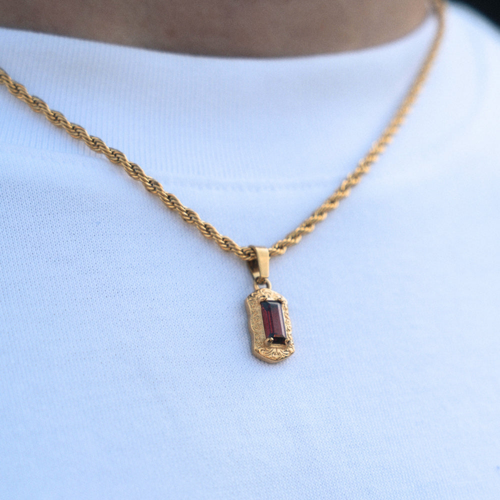 Gold necklace with a red gemstone pendant on a light blue background