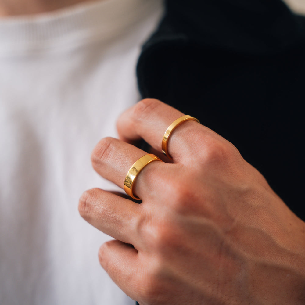 Close-up of a hand wearing two gold rings on a blurred background