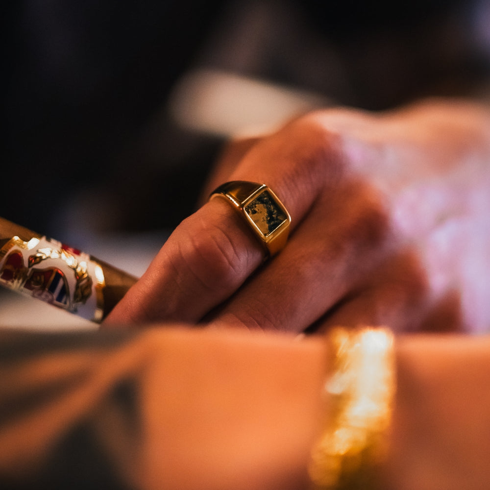 Close-up of a hand wearing a gold ring with a dark stone, holding a decorative object.