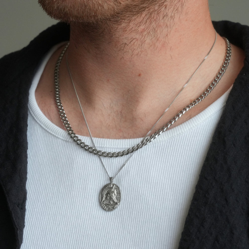 Person wearing a silver necklace with a pendant on a neutral background