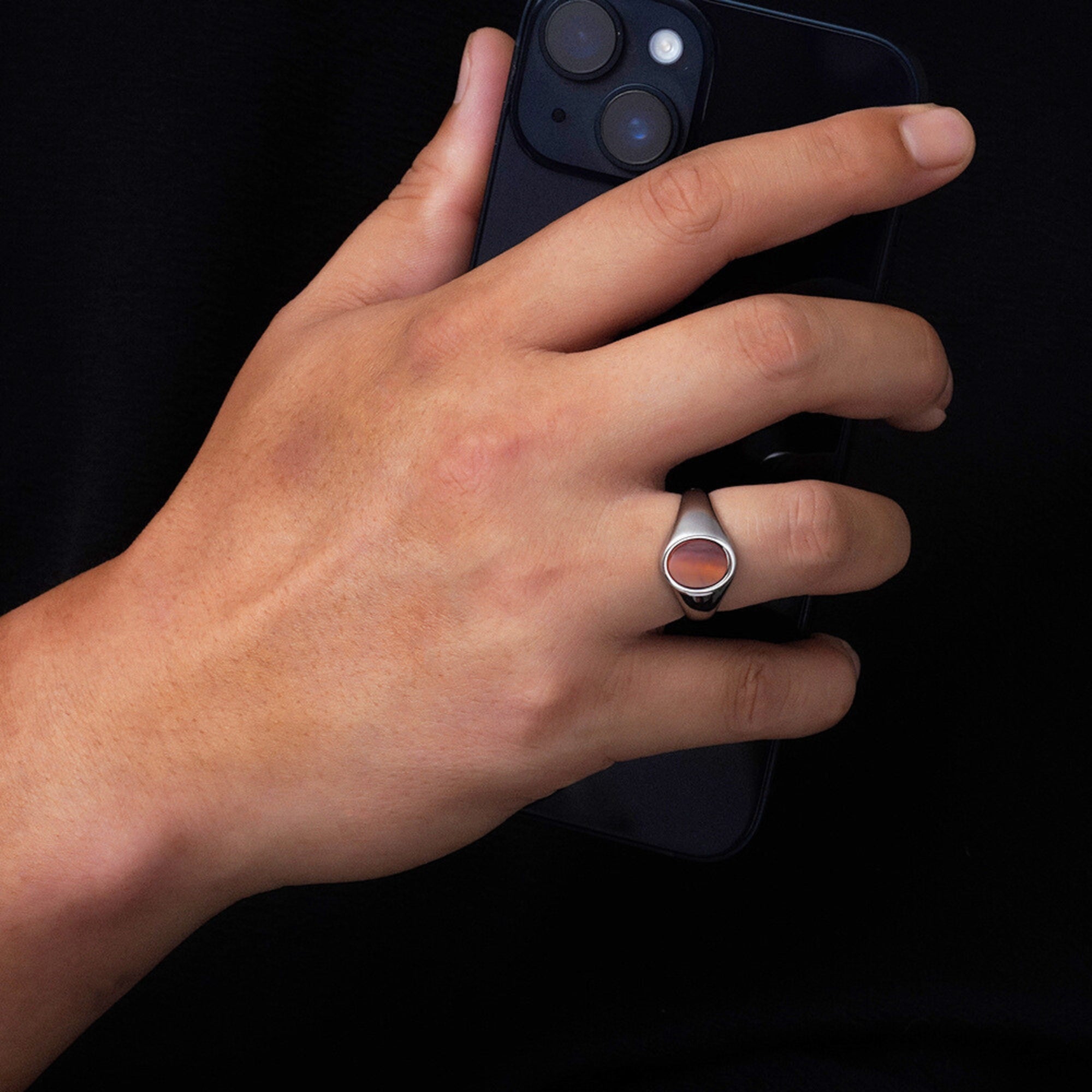 Hand wearing a ring holding a smartphone on a black background