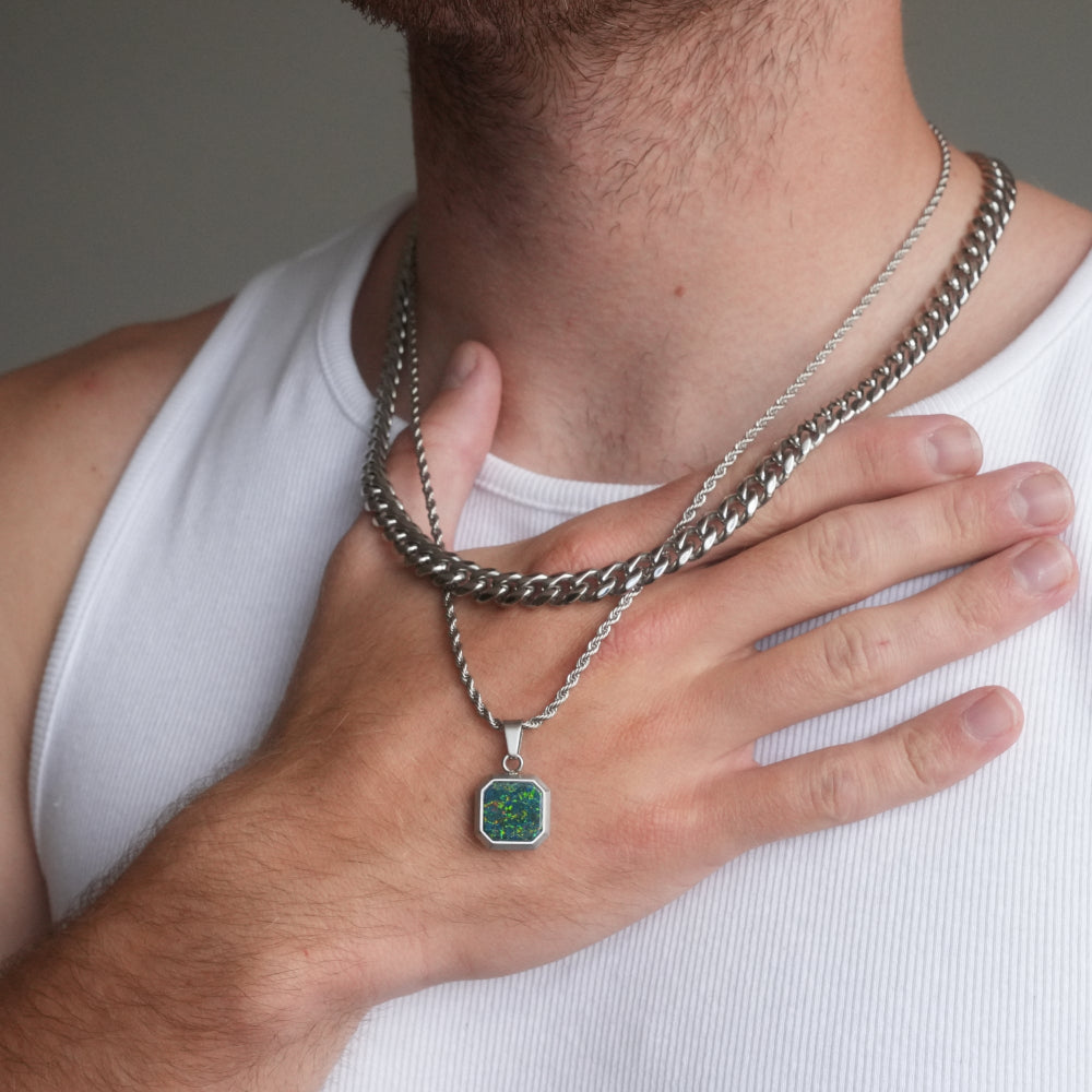 Man wearing a silver chain necklace with a green pendant on a plain background