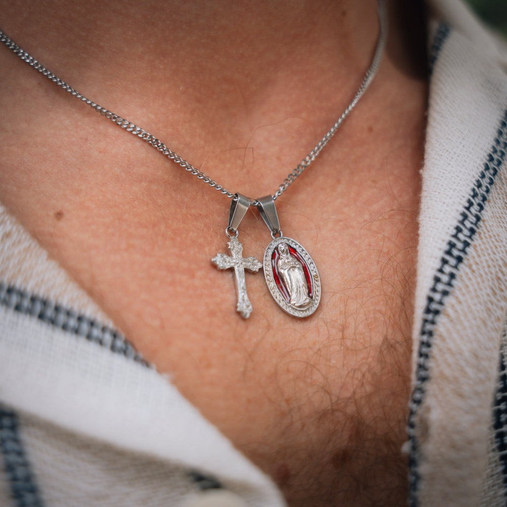 Close-up of a silver necklace with a cross and religious pendant on a person's neck.