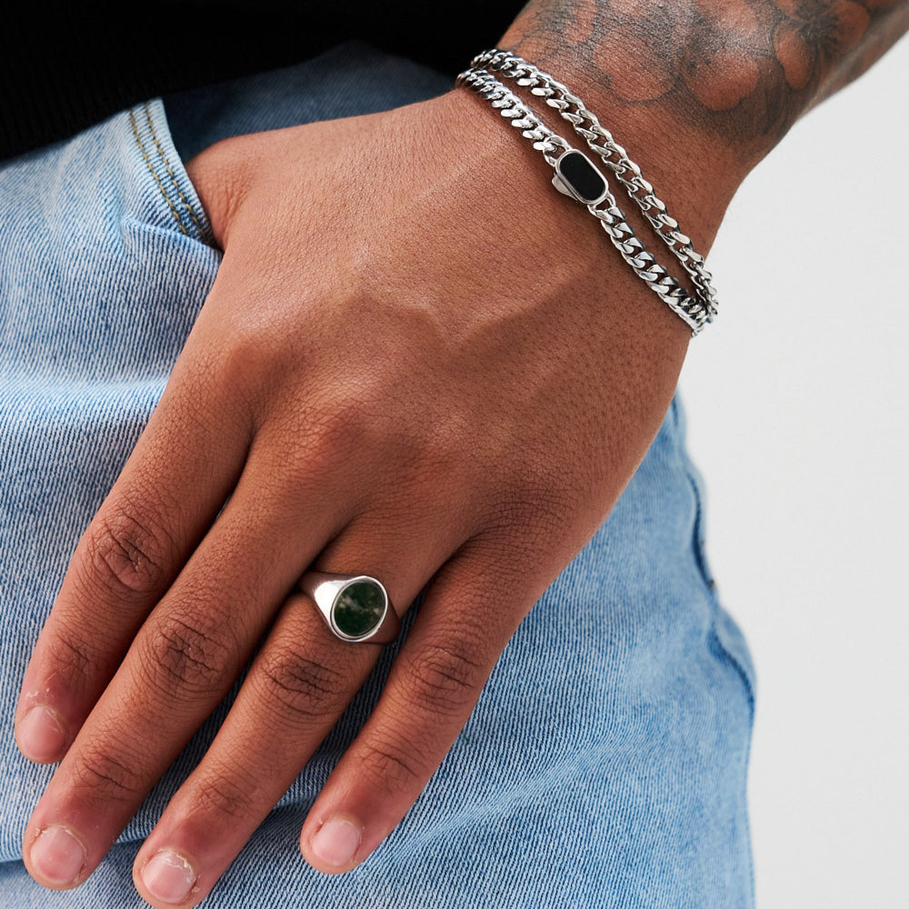 Hand wearing a silver ring with a green stone and multiple bracelets on a light blue denim background