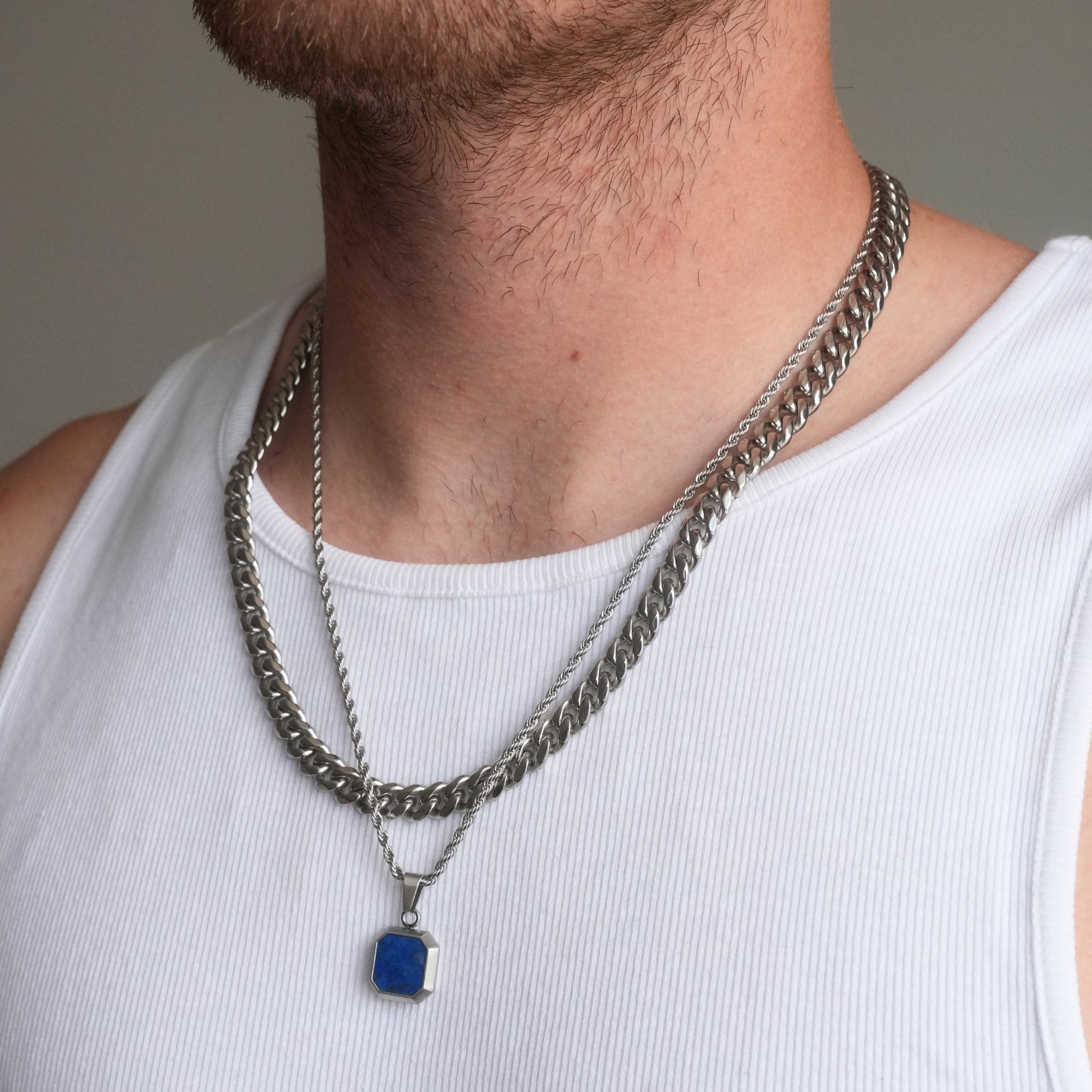 Close-up of a person wearing two silver chain necklaces with a blue pendant on a plain background