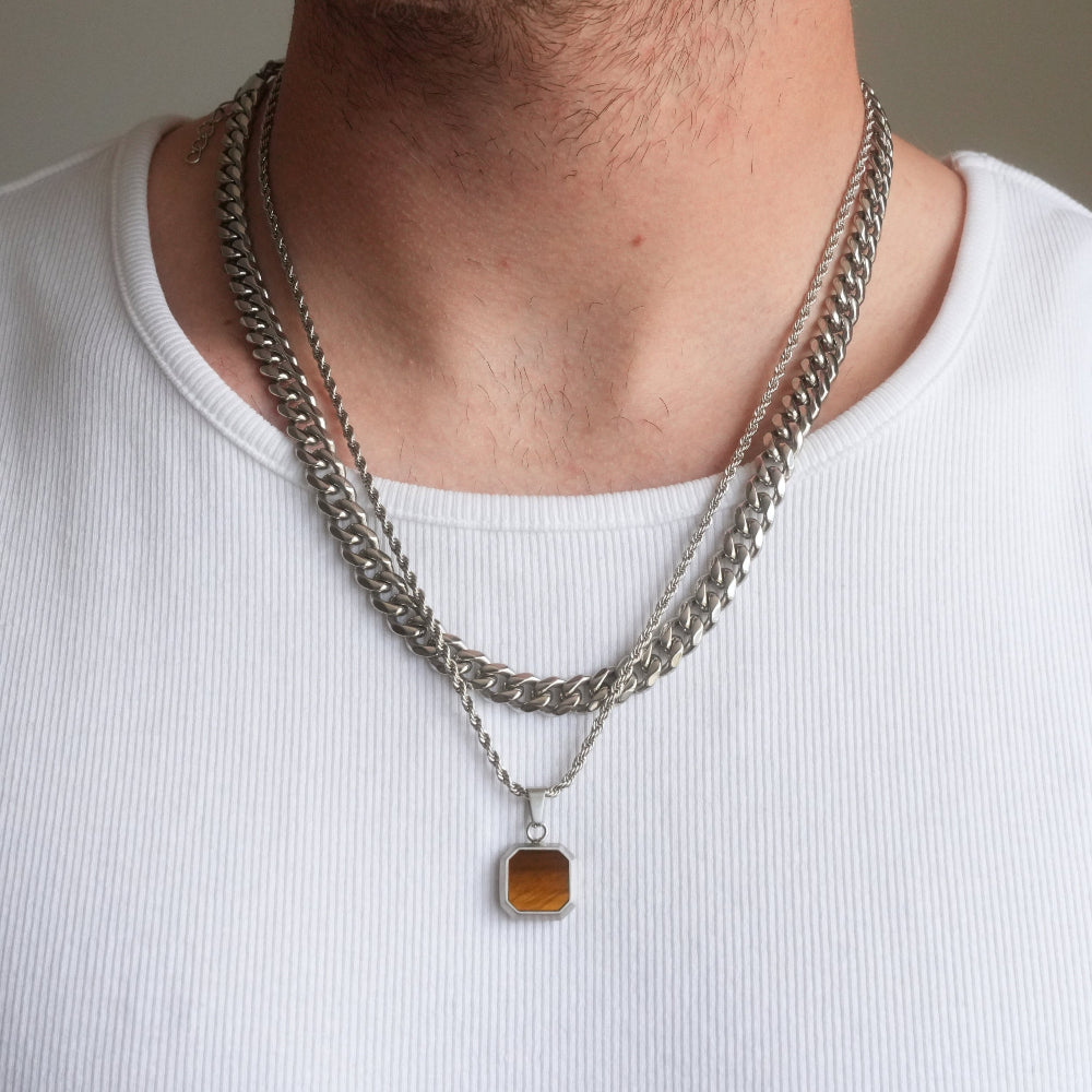 Close-up of a person wearing two silver chain necklaces with a pendant on a plain background