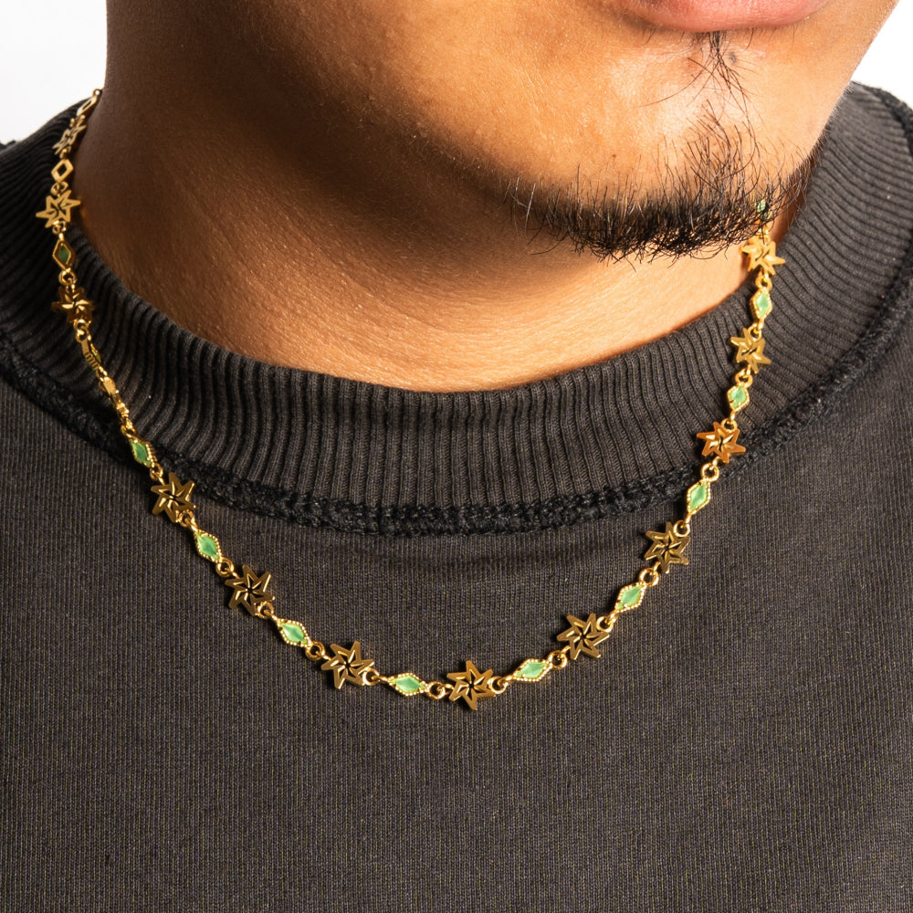 Gold necklace with star and green gemstone details worn by a person against a black background