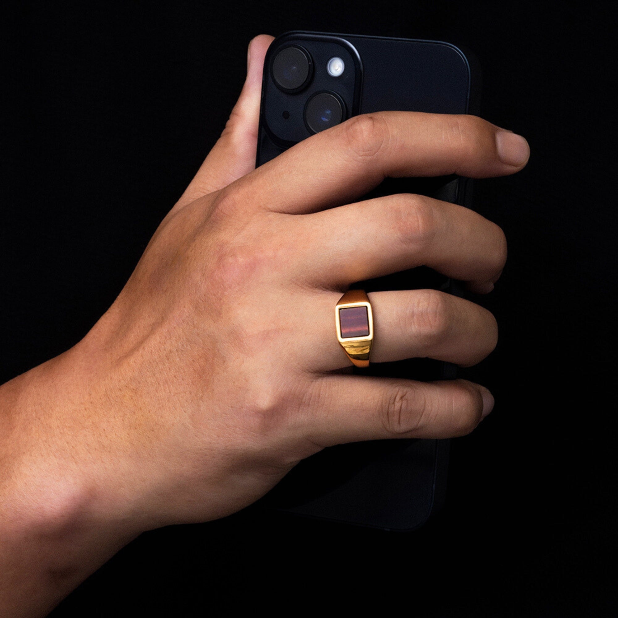 Hand holding a smartphone with a gold ring on a black background