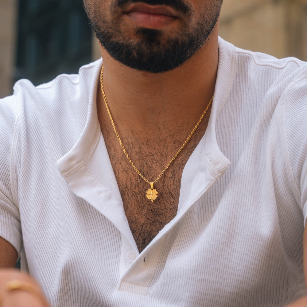 Man wearing a white shirt and gold necklace with a clover pendant.
