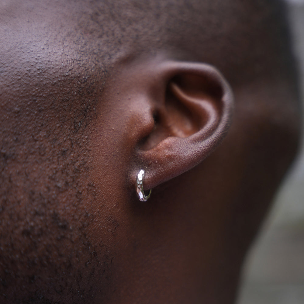 Close-up of an ear with a silver hoop earring on a dark background