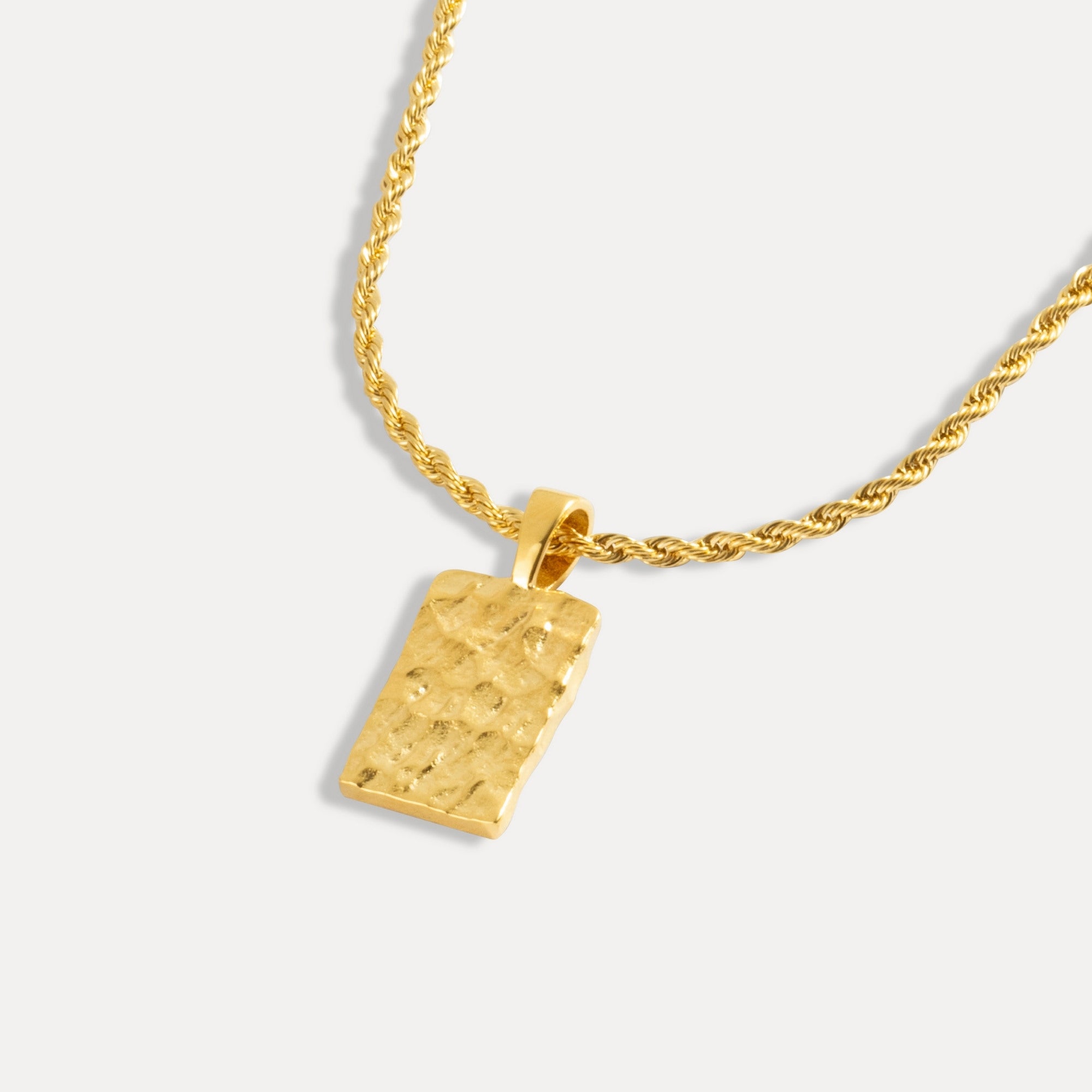 A gold-colored rectangular hammered pendant attached to a gold rope chain.