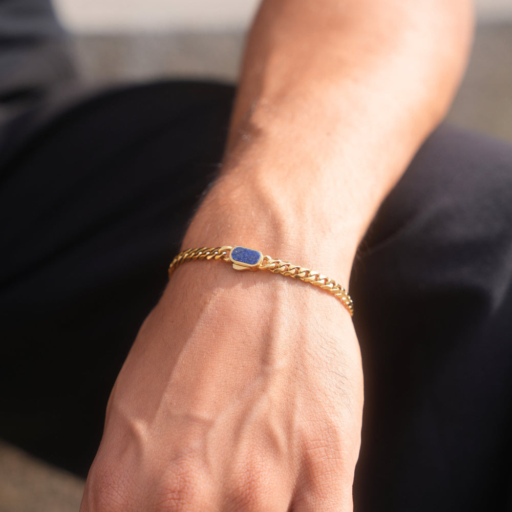Gold bracelet with a blue stone on a wrist against a blurred background