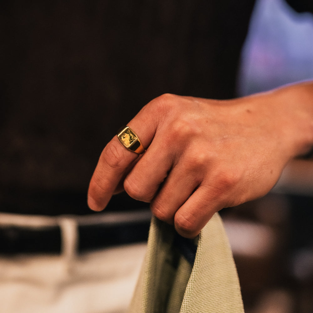 Hand wearing a gold ring holding a piece of fabric with a blurred background