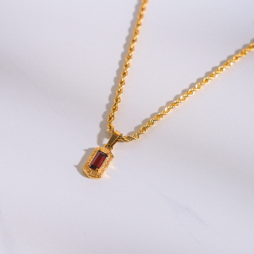Gold necklace with a red gemstone pendant on a white background