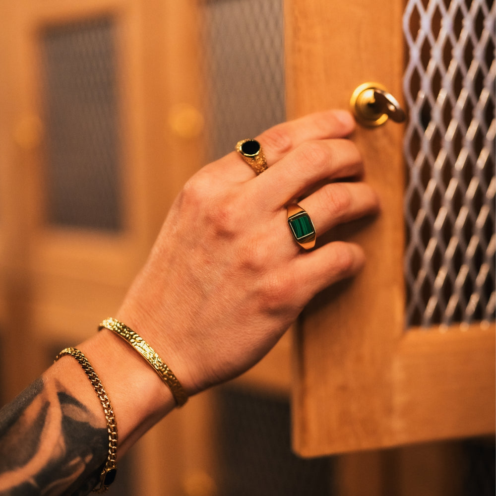 Hand with gold and emerald rings on a wooden surface