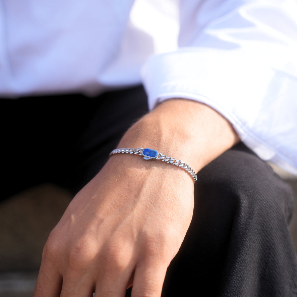 Close-up of a hand wearing a silver bracelet with a blue stone, against a blurred background.