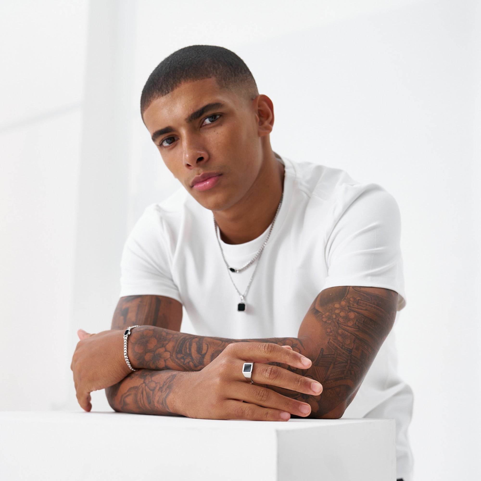 Man wearing a white t-shirt with tattoos on his arms against a plain background