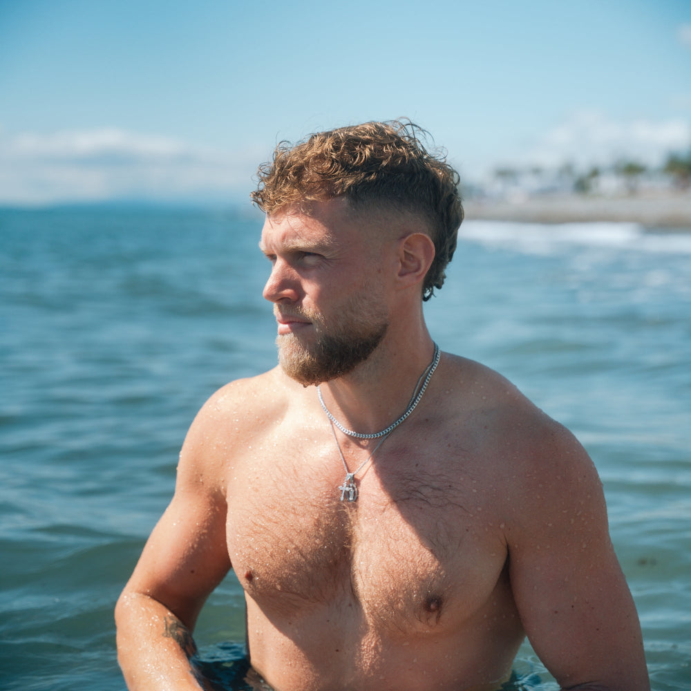 Man with a beard and necklace standing by the ocean
